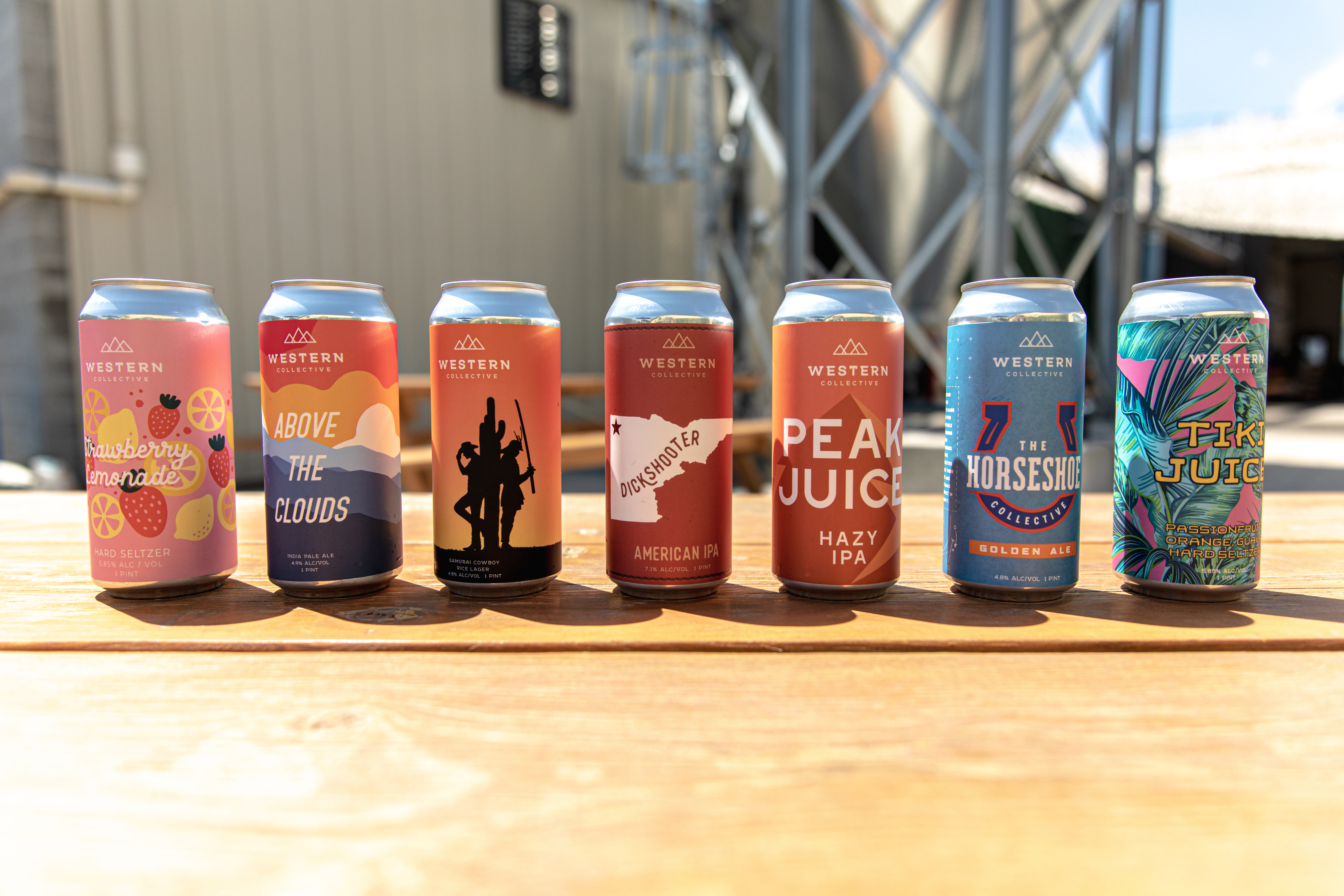 Western Collective beer lineup, seven cans on a picnic table at the brewery.